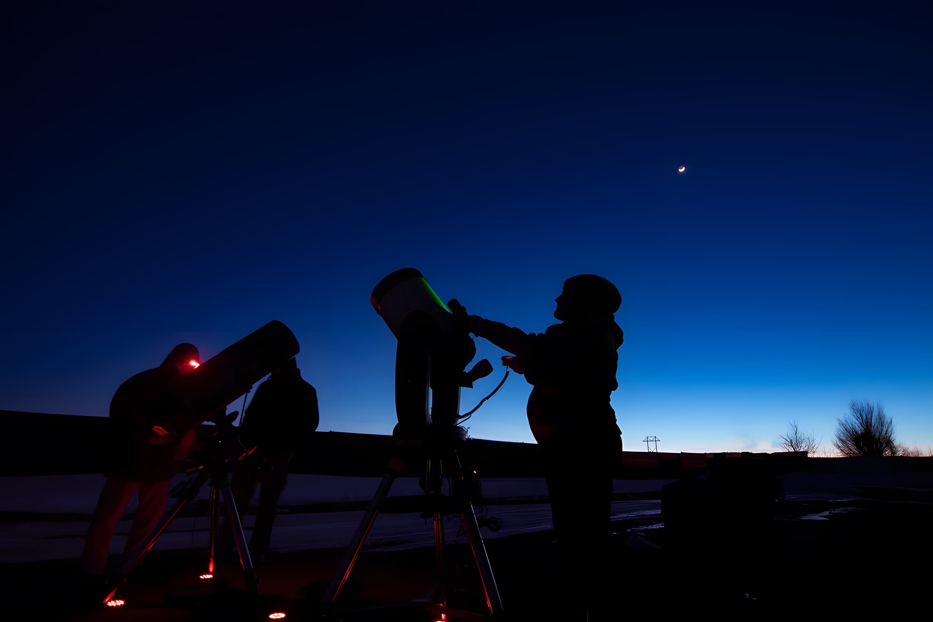 Three telescopes silhouetted against the twilight sky with a crescent moon at Bryce Canyon